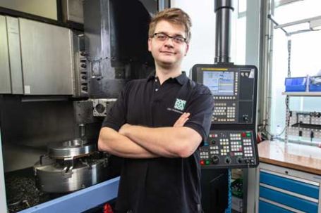 Lehrling vor Drehmaschine und Einstellungscomputer.